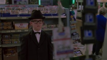 Movie still from “Varsity Blues” (1999), directed by Brian Robbins – A man in a suit and hat standing in front of a store; Medium shot, Over the shoulder angle