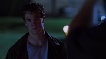 Movie still from “Varsity Blues” (1999), directed by Brian Robbins – A young man is looking at the camera while standing in the dark; Close Up shot, Over the shoulder angle