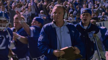 Movie still from “Varsity Blues” (1999), directed by Brian Robbins – A man in a blue baseball uniform is holding a book; Medium shot, Low angle