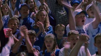 Movie still from “Varsity Blues” (1999), directed by Brian Robbins – A group of people sitting in a crowd clapping and applauding; Medium shot, High angle