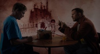 Movie still from “Venom: Let There Be Carnage” (2021), directed by Andy Serkis – Two men sitting at a table with a box of cereal; Medium shot, Low angle