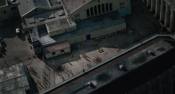 Movie still from “Venom: Let There Be Carnage” (2021), directed by Andy Serkis – An aerial view of people in orange jumpsuits in front of a building; Extreme Wide shot, Overhead angle