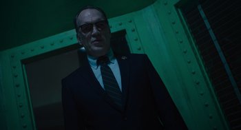 Movie still from “Venom: Let There Be Carnage” (2021), directed by Andy Serkis – A man in a suit and tie standing in front of a green wall; Medium shot, Low angle