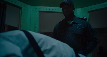 Movie still from “Venom: Let There Be Carnage” (2021), directed by Andy Serkis – A police officer standing next to a bed in a room; Medium shot, Over the shoulder angle
