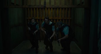 Movie still from “Venom: Let There Be Carnage” (2021), directed by Andy Serkis – A group of men holding guns in front of a wooden wall; Wide shot, Low angle