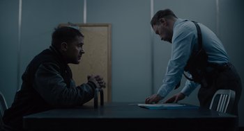 Movie still from “Venom: Let There Be Carnage” (2021), directed by Andy Serkis – Two men sitting at a table in front of each other; Medium shot, Over the shoulder angle