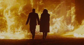 Movie still from “Venom: Let There Be Carnage” (2021), directed by Andy Serkis – A man and a woman holding hands as they walk away from a fire; Wide shot, Low angle