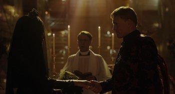 Movie still from “Venom: Let There Be Carnage” (2021), directed by Andy Serkis – A man in a priest's robe is holding a book; Medium shot, Over the shoulder angle