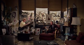 Movie still from “Vertigo” (1958), directed by Alfred Hitchcock – A man and a woman sitting in a chair in front of paintings; Wide shot, High angle