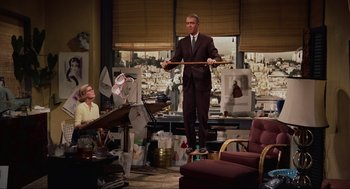 Movie still from “Vertigo” (1958), directed by Alfred Hitchcock – A man in a suit and tie holding a stick in a living room; Wide shot, Low angle