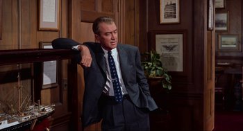 Movie still from “Vertigo” (1958), directed by Alfred Hitchcock – A man in a suit and tie leaning against a wall; Medium shot, Low angle