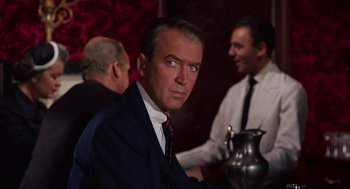 Movie still from “Vertigo” (1958), directed by Alfred Hitchcock – A man in a suit and tie sitting at a table; Close Up shot, Over the shoulder angle