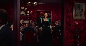 Movie still from “Vertigo” (1958), directed by Alfred Hitchcock – A woman in a black dress standing in front of a group of diners; Wide shot, Low angle