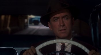 Movie still from “Vertigo” (1958), directed by Alfred Hitchcock – A man wearing a hat and a suit driving a car; Close Up shot, Over the shoulder angle