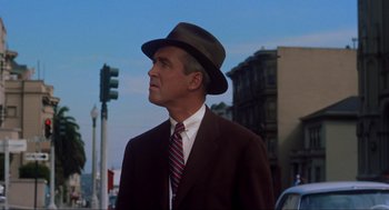 Movie still from “Vertigo” (1958), directed by Alfred Hitchcock – A man in a suit and hat standing on the side of the street; Close Up shot, Low angle