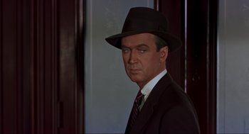 Movie still from “Vertigo” (1958), directed by Alfred Hitchcock – A man in a suit and hat is standing in front of a door; Close Up shot, Over the shoulder angle
