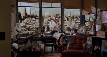Movie still from “Vertigo” (1958), directed by Alfred Hitchcock – A woman sitting on a stool in front of a large window; Wide shot, High angle