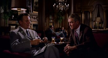 Movie still from “Vertigo” (1958), directed by Alfred Hitchcock – Two men in suits and ties sitting at a table with drinks in front of them; Medium shot, Over the shoulder angle