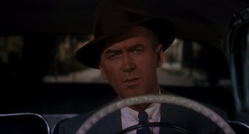 Movie still from “Vertigo” (1958), directed by Alfred Hitchcock – A man wearing a hat sitting in the driver's seat of a car; Close Up shot, Over the shoulder angle