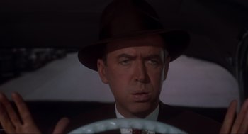 Movie still from “Vertigo” (1958), directed by Alfred Hitchcock – A person wearing a suit and a hat driving; Close Up shot, Over the shoulder angle