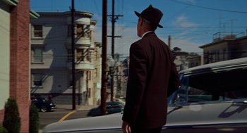 Movie still from “Vertigo” (1958), directed by Alfred Hitchcock – A man in a suit and hat standing on the side of the road; Wide shot, Low angle