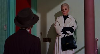 Movie still from “Vertigo” (1958), directed by Alfred Hitchcock – A woman in a white coat and a man in a black hat; Medium shot, Over the shoulder angle