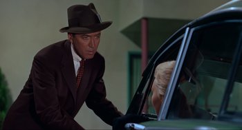 Movie still from “Vertigo” (1958), directed by Alfred Hitchcock – A man in a suit and a hat leaning on a car door; Medium shot, Over the shoulder angle