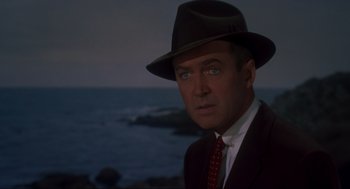 Movie still from “Vertigo” (1958), directed by Alfred Hitchcock – A man in a suit and a hat looking at the camera; Close Up shot, Over the shoulder angle