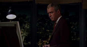 Movie still from “Vertigo” (1958), directed by Alfred Hitchcock – A man in a suit standing in front of a window; Medium shot, Over the shoulder angle
