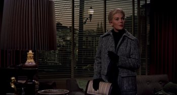 Movie still from “Vertigo” (1958), directed by Alfred Hitchcock – A woman standing in front of a window holding a purse; Medium shot, Over the shoulder angle