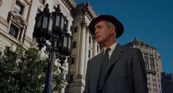 Movie still from “Vertigo” (1958), directed by Alfred Hitchcock – A man in a suit and hat standing next to a street light; Medium shot, Low angle