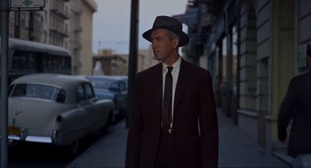 Movie still from “Vertigo” (1958), directed by Alfred Hitchcock – A man in a suit and hat standing on the side of the street; Medium shot, Low angle