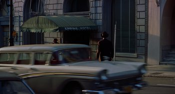 Movie still from “Vertigo” (1958), directed by Alfred Hitchcock – A woman standing on the side of the road next to cars; Wide shot, Over the shoulder angle
