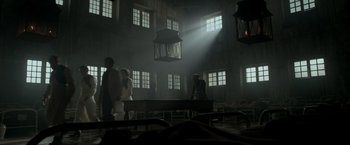 Movie still from “Victor Frankenstein” (2015), directed by Paul McGuigan – A group of people standing around a table in a room; Wide shot, Low angle