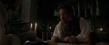 Movie still from “Victor Frankenstein” (2015), directed by Paul McGuigan – A man sitting at a table with a knife in his hand; Medium shot, Over the shoulder angle