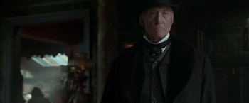 Movie still from “Victor Frankenstein” (2015), directed by Paul McGuigan – An older man in a black hat and a black coat; Close Up shot, Low angle