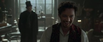 Movie still from “Victor Frankenstein” (2015), directed by Paul McGuigan – A man in a vest and a hat is smiling for the camera; Close Up shot, Over the shoulder angle