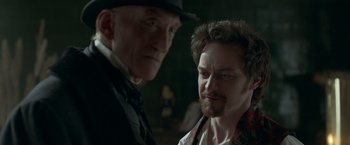 Movie still from “Victor Frankenstein” (2015), directed by Paul McGuigan – Two men standing next to each other in front of a dark background; Close Up shot, Over the shoulder angle