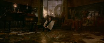 Movie still from “Victor Frankenstein” (2015), directed by Paul McGuigan – A man holding a piece of paper sitting on the floor of a living room; Wide shot, High angle