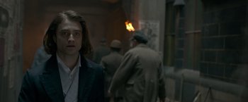 Movie still from “Victor Frankenstein” (2015), directed by Paul McGuigan – A young man standing next to a group of men; Close Up shot, Over the shoulder angle