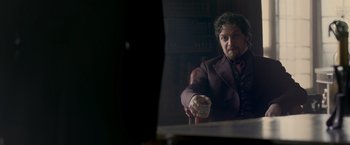 Movie still from “Victor Frankenstein” (2015), directed by Paul McGuigan – A man sitting in front of a mirror holding a cup; Medium shot, Over the shoulder angle
