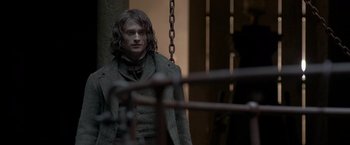 Movie still from “Victor Frankenstein” (2015), directed by Paul McGuigan – A man standing in front of a metal fence; Medium shot, Over the shoulder angle