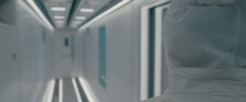 Movie still from “Voyagers” (2021), directed by Neil Burger – A person in a white lab coat is standing in a white room; Extreme Close Up shot, Over the shoulder angle