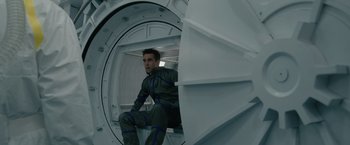 Movie still from “Voyagers” (2021), directed by Neil Burger – A man sitting inside of an enclosed space station; Medium shot, Overhead angle