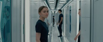Movie still from “Voyagers” (2021), directed by Neil Burger – A woman standing in a hallway with two men standing in the background; Medium shot, Over the shoulder angle