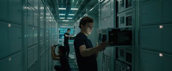 Movie still from “Voyagers” (2021), directed by Neil Burger – A man in black shirt holding a computer monitor; Medium shot, Low angle
