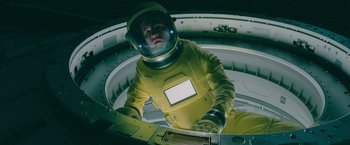 Movie still from “Voyagers” (2021), directed by Neil Burger – A man in a space suit is inside of a space station; Medium shot, Overhead angle