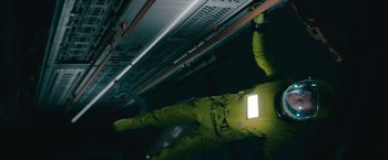 Movie still from “Voyagers” (2021), directed by Neil Burger – A man in a yellow suit is standing in a dark room; Medium shot, Overhead angle