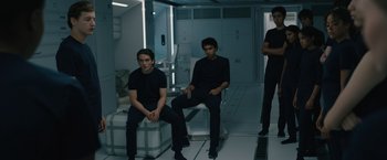 Movie still from “Voyagers” (2021), directed by Neil Burger – A group of men sitting on a chair in a room; Medium shot, Low angle