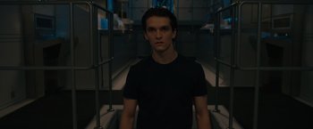Movie still from “Voyagers” (2021), directed by Neil Burger – A man in a black t - shirt standing in a room; Medium shot, Low angle